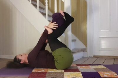 Person lying on a mat holding feet in a supine yoga stretch for 4 maneder.