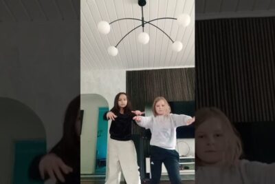 Two Children Dancing in a Modern Living Room — 8 maaliskuuta Lifestyle Photo showing two kids dancing in a minimalist living room with a modern multi-globe ceiling light, vertical wood paneling and a wall-mounted TV.