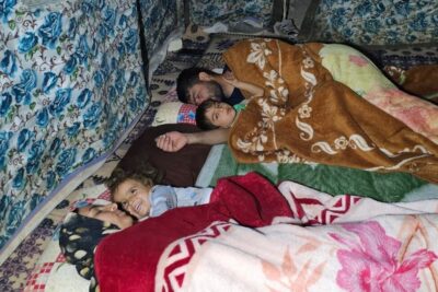 Adults and children lying closely on layered floral and patterned blankets on the floor, a bestemme