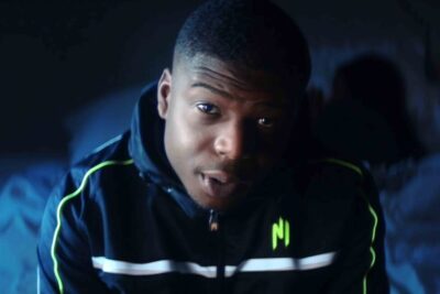 Close-up portrait of a young man wearing a neon-accented jacket in low blue light a fremme 1