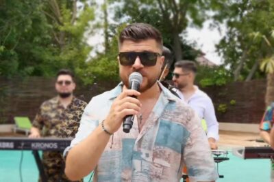Male singer wearing sunglasses holding a microphone in a poolside band performance a ta 1.
