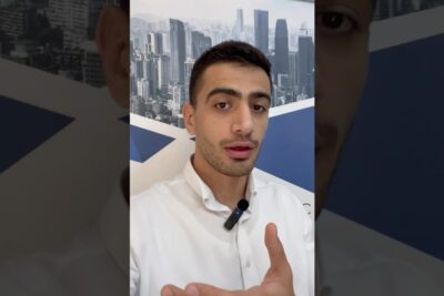 Man in a white shirt wearing a lapel microphone speaking about abent handelssystem against a city skyline poster.