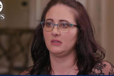 Close-up of a concerned woman with glasses in a news interview related to abort ar 6.
