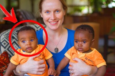 Smiling caregiver holding two infants in matching orange shirts with a red circle highlighting one infant, adoptoida lapsia