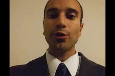 Close-up of a man in a suit and tie speaking toward the camera for afstemning 16 ars