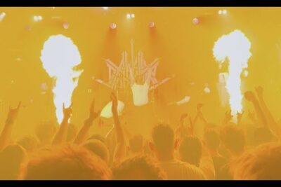 Crowd facing a brightly lit stage with towering flames and intense yellow lighting aktiv dodshjelp 4.