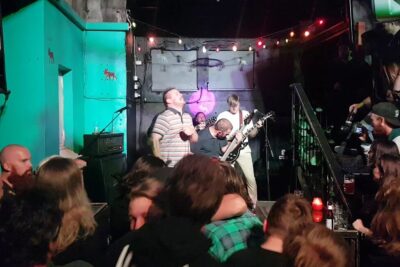 Energetic band performing to a packed small venue with string lights and loud crowd, aktiv dodshjelp 5.