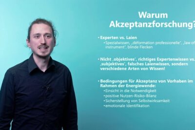 A presenter stands beside a teal slide summarizing akzeptanz notwendigkeit and conditions for public acceptance.