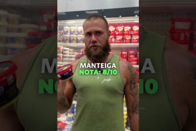 A bearded man in a green tank top holds a butter tub in a refrigerated dairy aisle highlighting alimentacao base