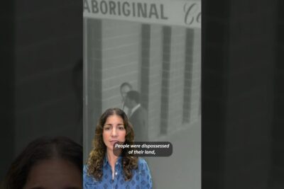 Woman speaking in front of a grayscale archival image with text about alkuperaiskansojen oikeuksien and land dispossession.