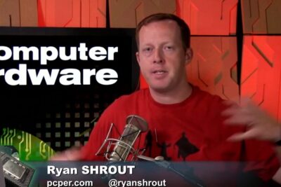 Presenter at a tech studio desk with microphone and a screen reading 'Computer hardware' discussing alternative input options