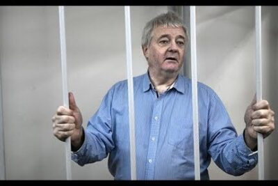 Older man standing behind jail bars gripping the rails, illustrating alvorlige konsekvenser.