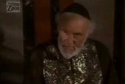 Close-up portrait of an elderly bearded man wearing a dark cap and ornate embroidered robe, anas jesus 2.