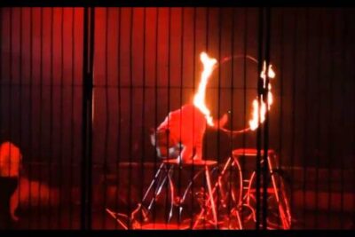 Lion leaping through a flaming hoop inside a barred cage under red circus lighting, animales circos 1.