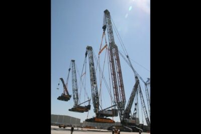 Multiple lattice-boom cranes lifting large tracked mining buckets against a clear sky, apen gruveutvinning 1