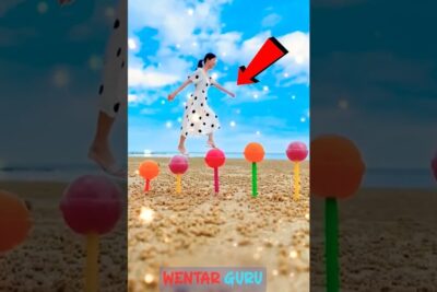 Woman in a white polka dot dress jumping over bright lollipop-like stakes on a sandy beach, highlighting arbetar for.