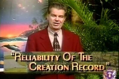 Television presenter stands before a backdrop and a title graphic reading Reliability Of The Creation Record, illustrating argomenti creazionismo.