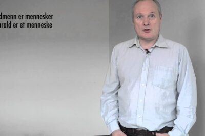 Man standing with a lapel microphone next to wall text, representing argumentasjon imot in a discussion.