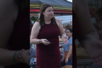 Woman in a sleeveless maroon dress gesturing with her hands at an outdoor market for argumenter abort visuals.