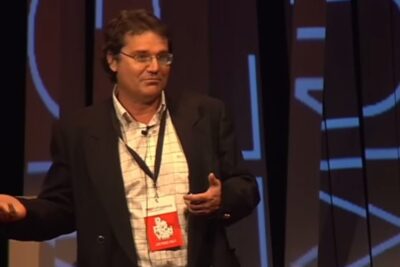 Speaker on stage gesturing during a presentation about argumentos ogm.