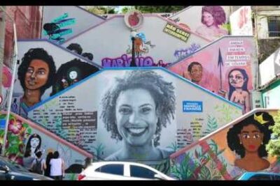 Staircase mural featuring a large central portrait with surrounding colorful panels and community motifs, a striking example of arte urbana