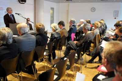 Audience seated in rows listening to a speaker at det 5 during a presentation.