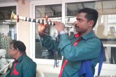 Man in green shirt playing a long striped wind instrument ata kott 1