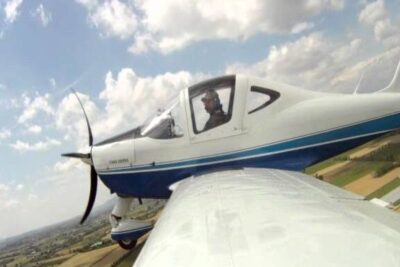 Small single-engine propeller plane banking over fields during atterrare controvento maneuver.