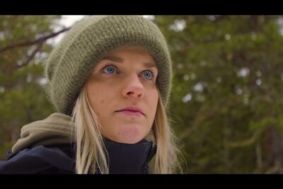 Close-up portrait of a woman in a green beanie outdoors conveying calm determination to auttaa ihmisia.