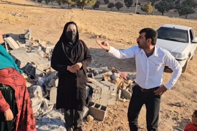 Three adults and a child near broken concrete blocks in a dry field discussing aid and reconstruction, auttaa meita 13