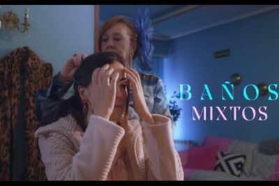 Two women in a cozy dressing area as one adjusts the other's hair under a banos mixtos sign.