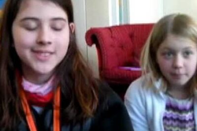 Two children seated on a living-room sofa, one smiling with eyes closed and the other looking at the camera, illustrating barnets rattigheter 1.