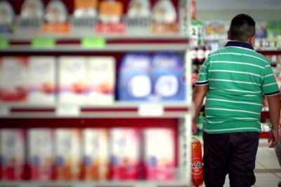 Shopper in a supermarket aisle holding a large bottle of bebidas azucaradas.