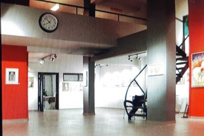 Open modern gallery interior with red accent walls, sculptural chair and spiral staircase suitable for bed rfnisse staging