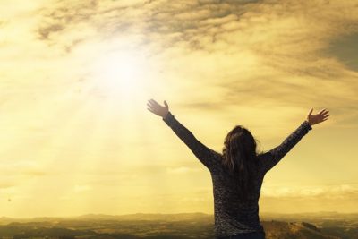 Silhouetted person standing on a hill with arms raised toward a glowing sunrise symbolizing hope and solidarity bekaemp mobning staa op imod daarlig behandling eller forkort det i faellesskab.