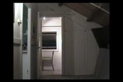Dim loft interior with a doorway opening to a small room featuring a single chair and window, bekampelse terrorisme.