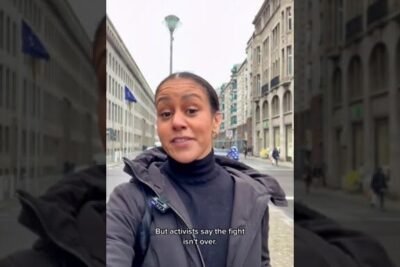 Woman recording a selfie-style video on a city street discussing ber rassismus with on-screen subtitle visible.