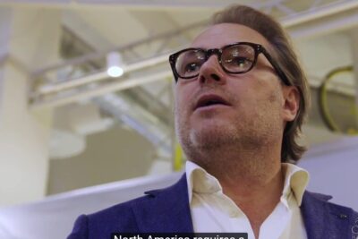 Close-up of a man in glasses and blazer at an indoor event representing beskytte forbrugerne