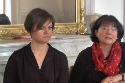 Two women seated at a table in a meeting room by an ornate mirror, besoins educatifs