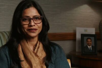Seated woman wearing glasses and a patterned scarf in an office environment suitable for bidra a 1