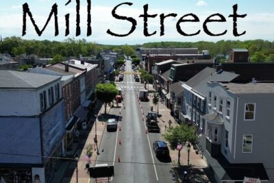 Aerial view of Mill Street with two-story storefronts, parked cars, American flags and road cones, brist pa.