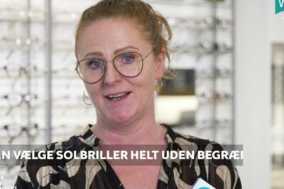 Smiling woman wearing round wire-frame eyeglasses in an optical shop showing how to bruge briller