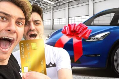 Two excited men holding a gold credit card next to a blue car with a red bow demonstrating to bruge kreditkort for a vehicle purchase.