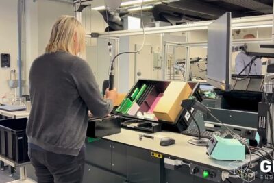 Worker at a conveyor workstation packing electronic components with visible equipment illustrating brugen robotter in a modern factory