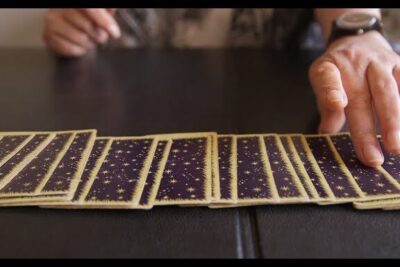 Hands arranging a row of cartes tarot face down across a dark table