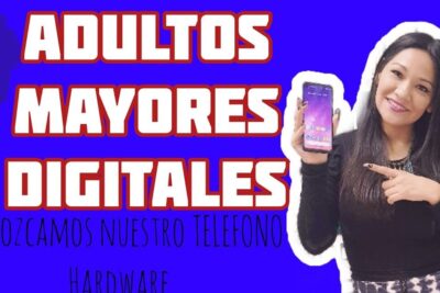 Smiling woman holding a smartphone and pointing to it while promoting a celular clase for older adults.
