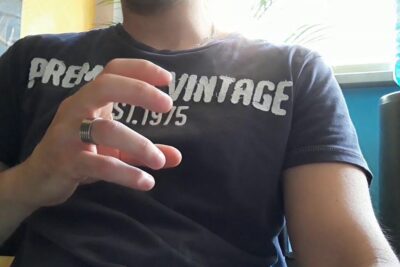 Close-up of person wearing a dark vintage t-shirt showing a hand with a metal ring, circoncisione ridurre