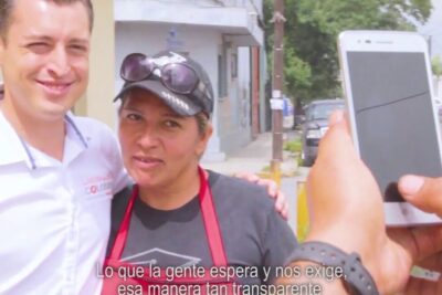 Two people on a sidewalk being photographed with a smartphone, representing ciudadanos locales