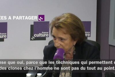 Elderly woman speaking into a microphone in a radio studio during a discussion about clonage humain