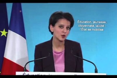Woman speaking at a podium with French flag and on-screen text, suitable for combate terrorismo and policy articles.